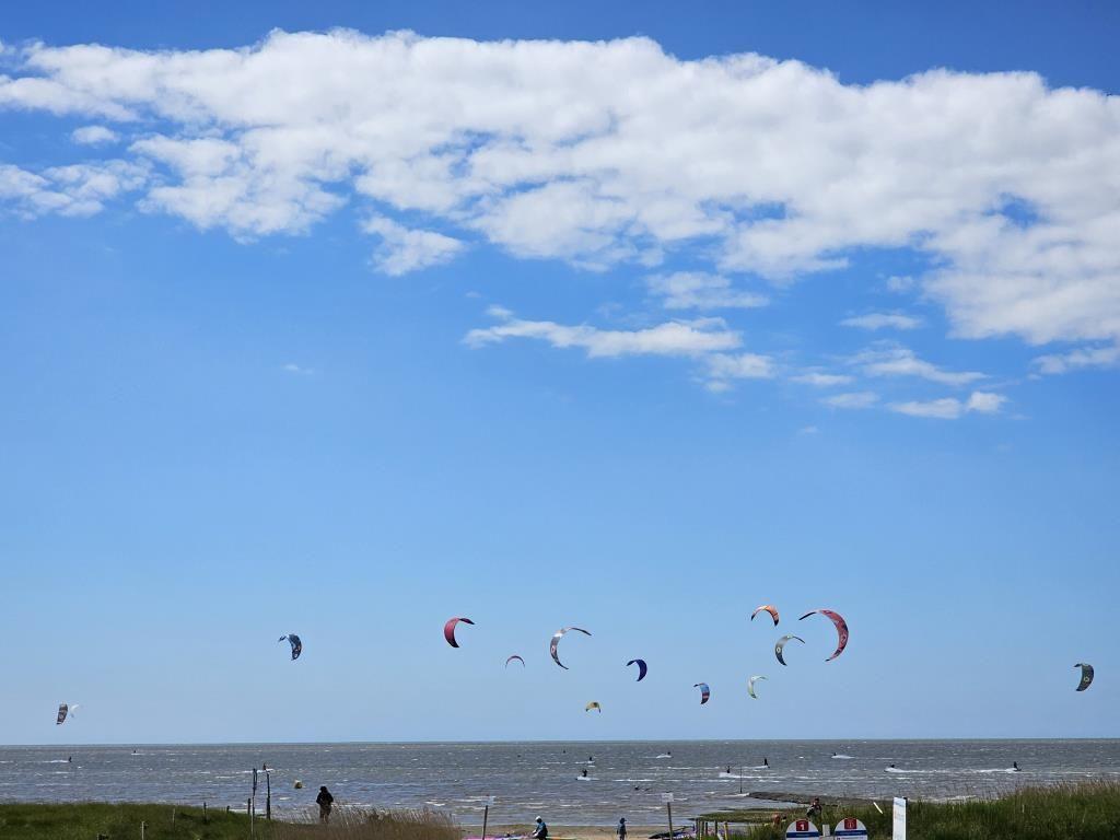 Kitesurfing auf dem Meer unter blauem Himmel mit weißen Wolken.