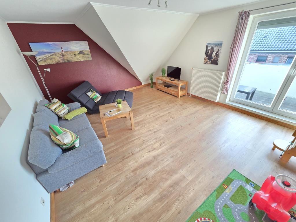 Wohnzimmer mit Sofa, Couchtisch und TV. Holzboden und große Fenster.