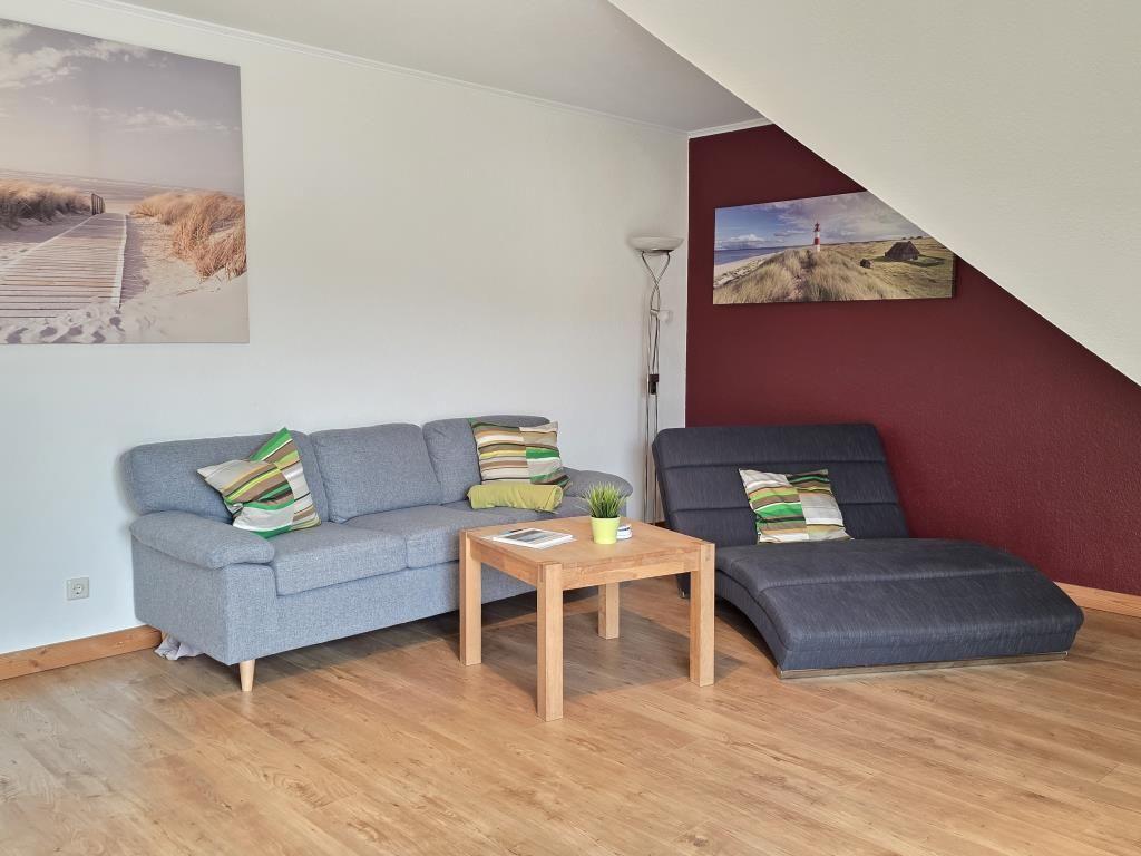 Wohnzimmer mit grauem Sofa, Holztisch und Wandbildern