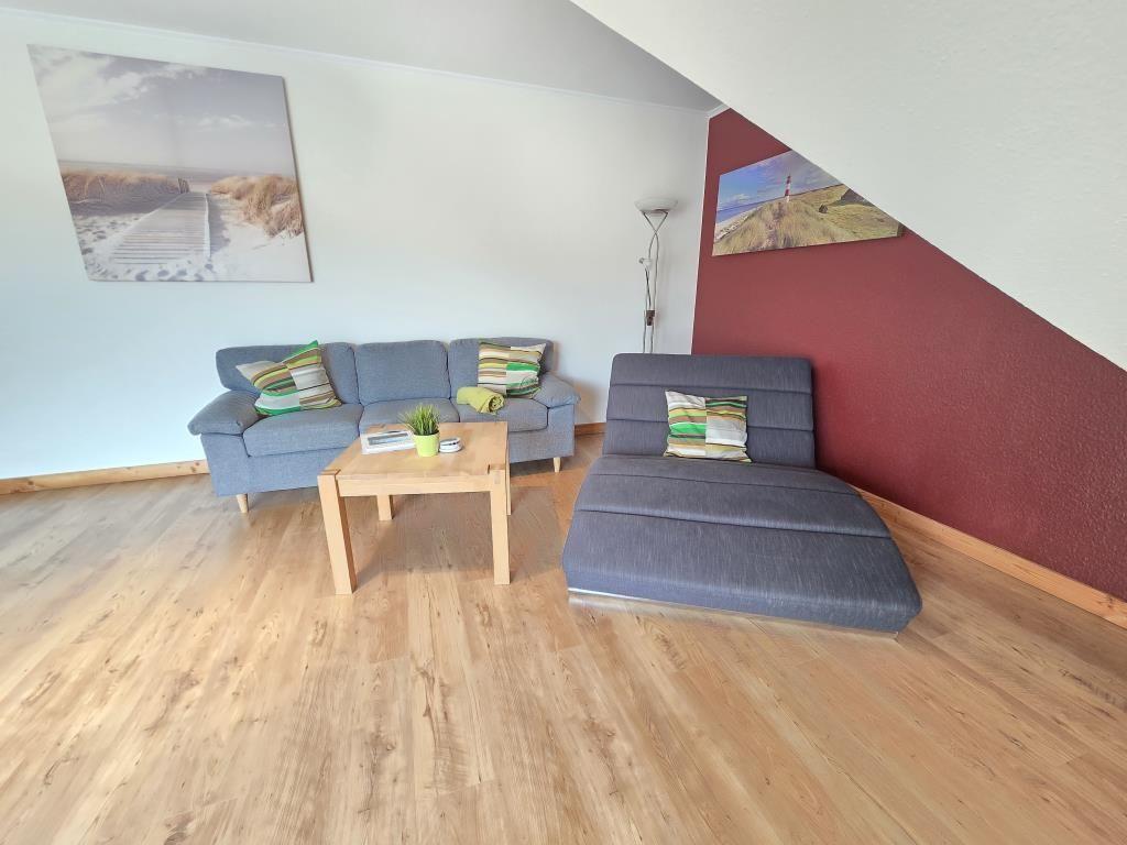 Wohnzimmer mit grauem Sofa, Couchtisch und Holzboden unter schräger Decke.
