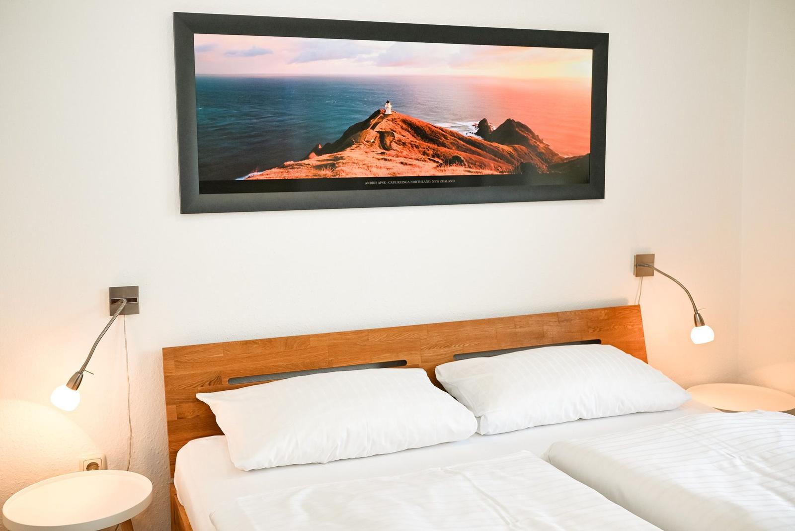 Schlafzimmer mit Doppelbett, Holz-Kopfteil und Wandbild an der Wand.