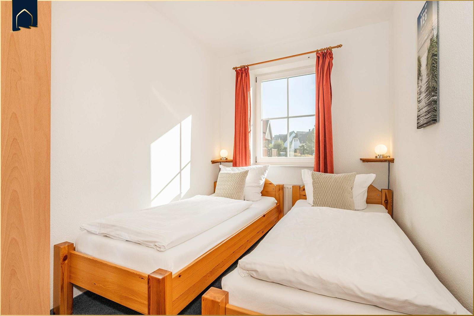 Zwei Einzelbetten mit weißen Bettwäschen und Holzrahmen. Fenster mit roten Vorhängen.