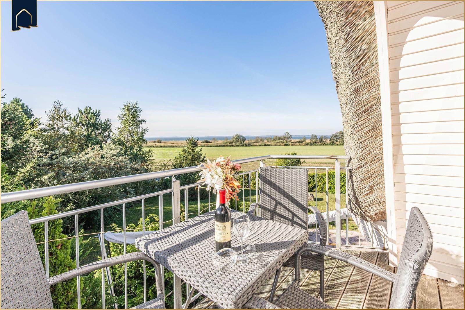 Terrasse mit Tisch, Stühlen und Weinkrug. Blick auf grüne Wiesen und Bäume.