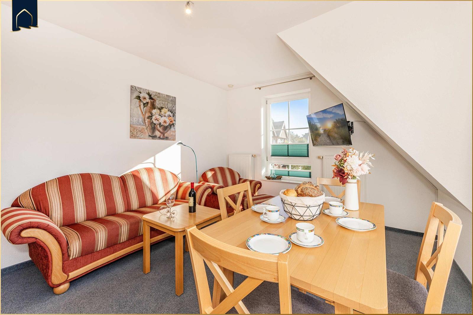 Wohn- und Essbereich mit Sofa, Tisch und Fenster. Wandbild und TV montiert.