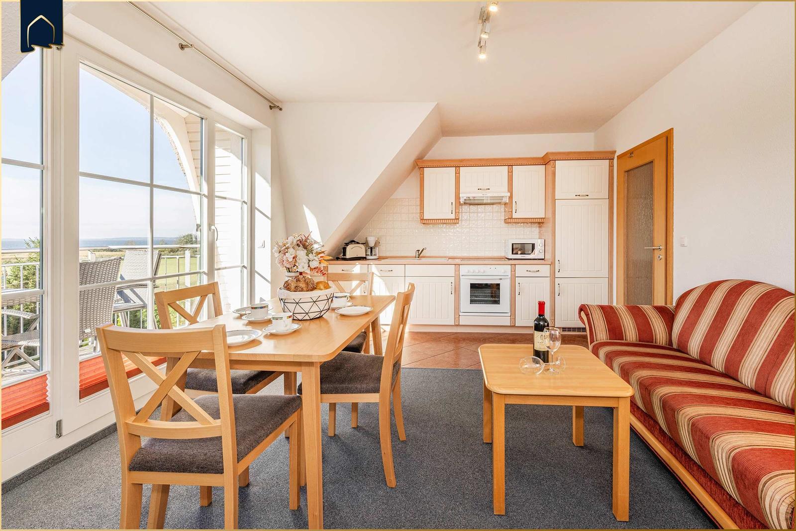 Wohnküche mit Essbereich und Balkonblick. Sofa, Tisch und Küchenschränke sichtbar.