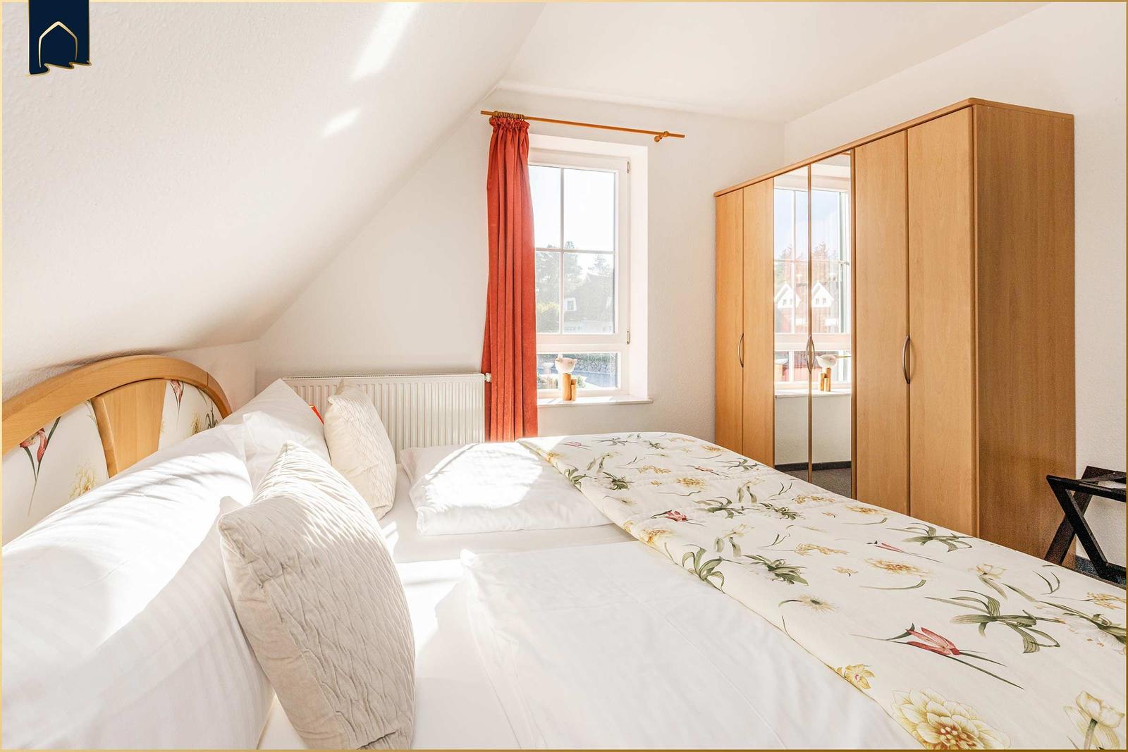 Schlafzimmer mit Dachschräge, Bett, Kleiderschrank und Fenster mit roter Vorhang.