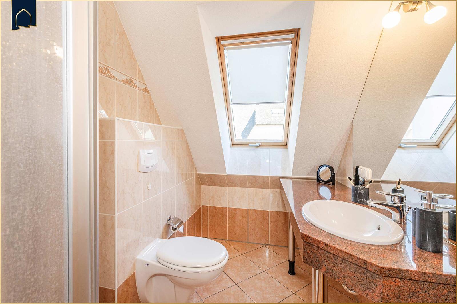 Badezimmer mit Toilette, Waschbecken und Dachfenster. Fliesenwand und Boden.