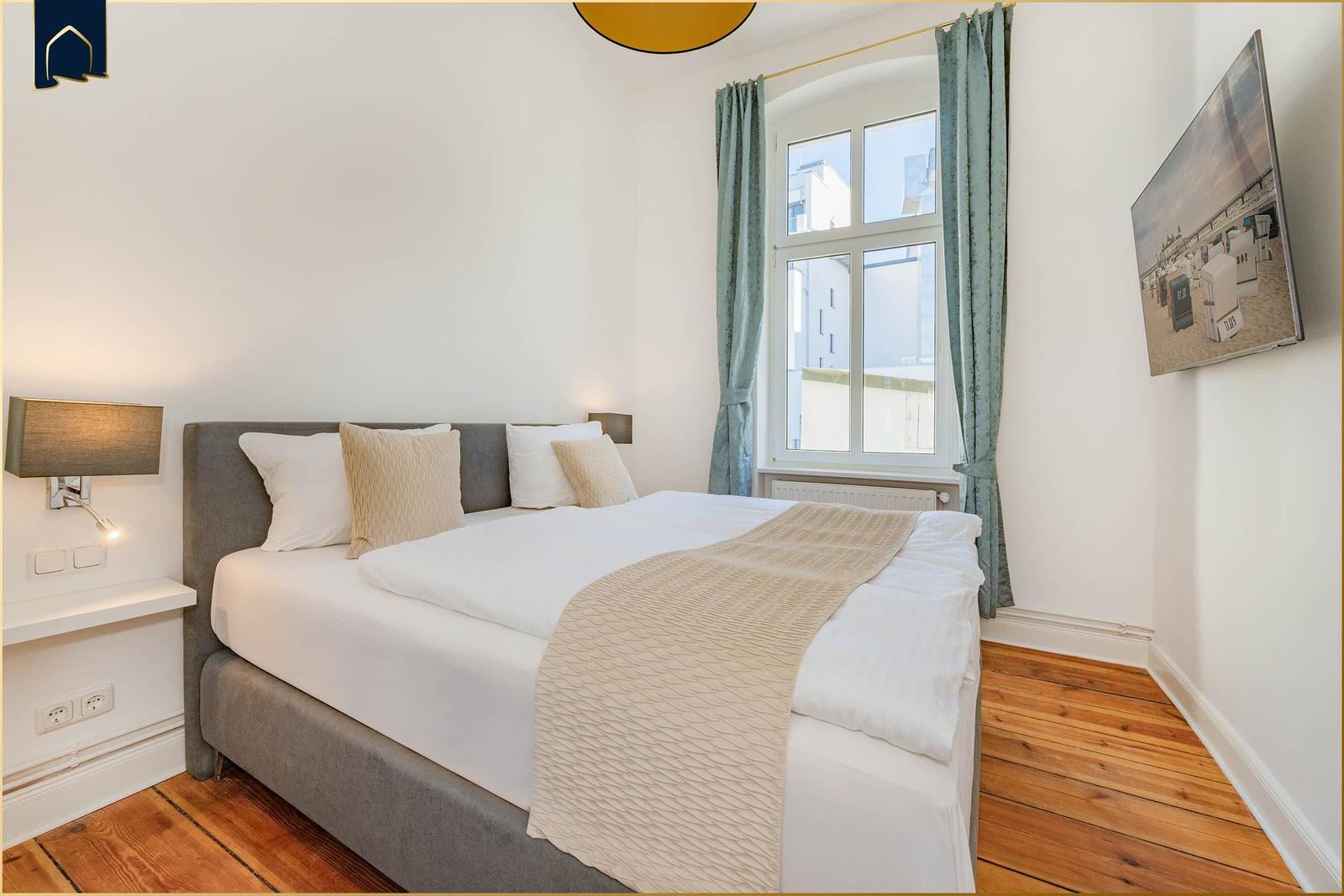 Schlafzimmer mit Doppelbett, Fenster, Vorhängen und Wandbild.