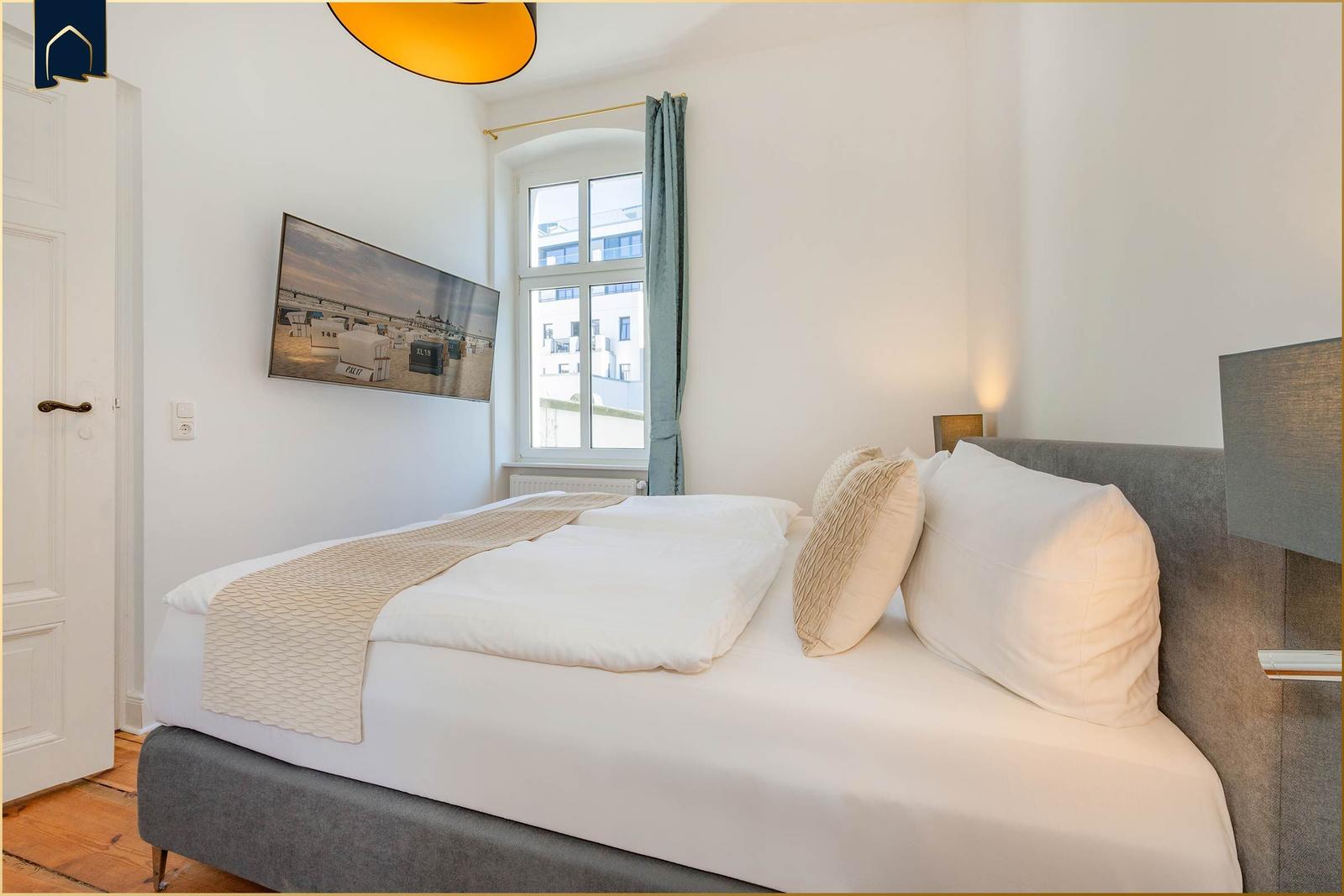 Schlafzimmer mit Bett, Fenster und Wandbild. Holzboden und moderne Beleuchtung.