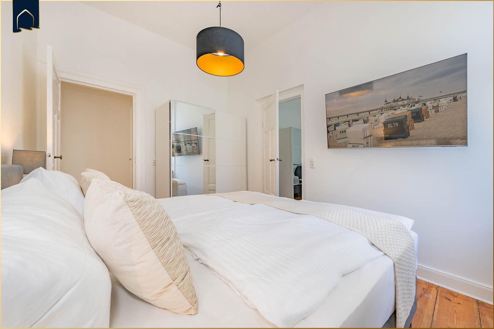 Schlafzimmer mit Bett, Wandbild und Deckenleuchte.