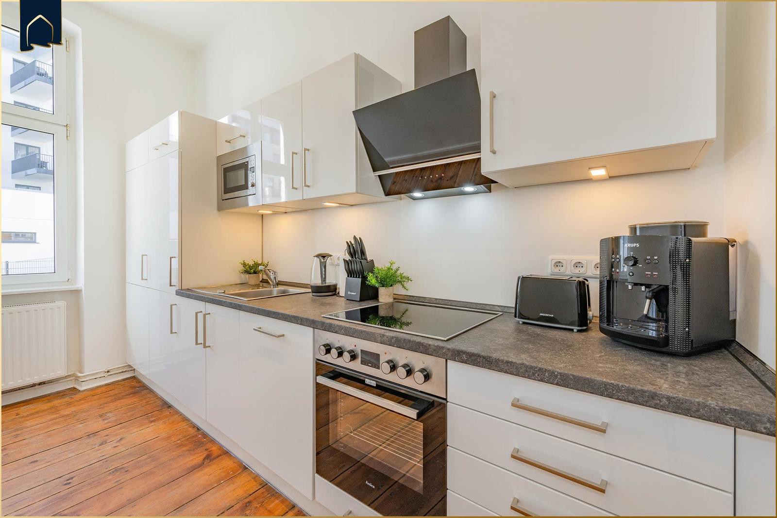 Moderne Küche mit weißen Schränken, Edelstahlgeräten und dunklem Arbeitsplatte.