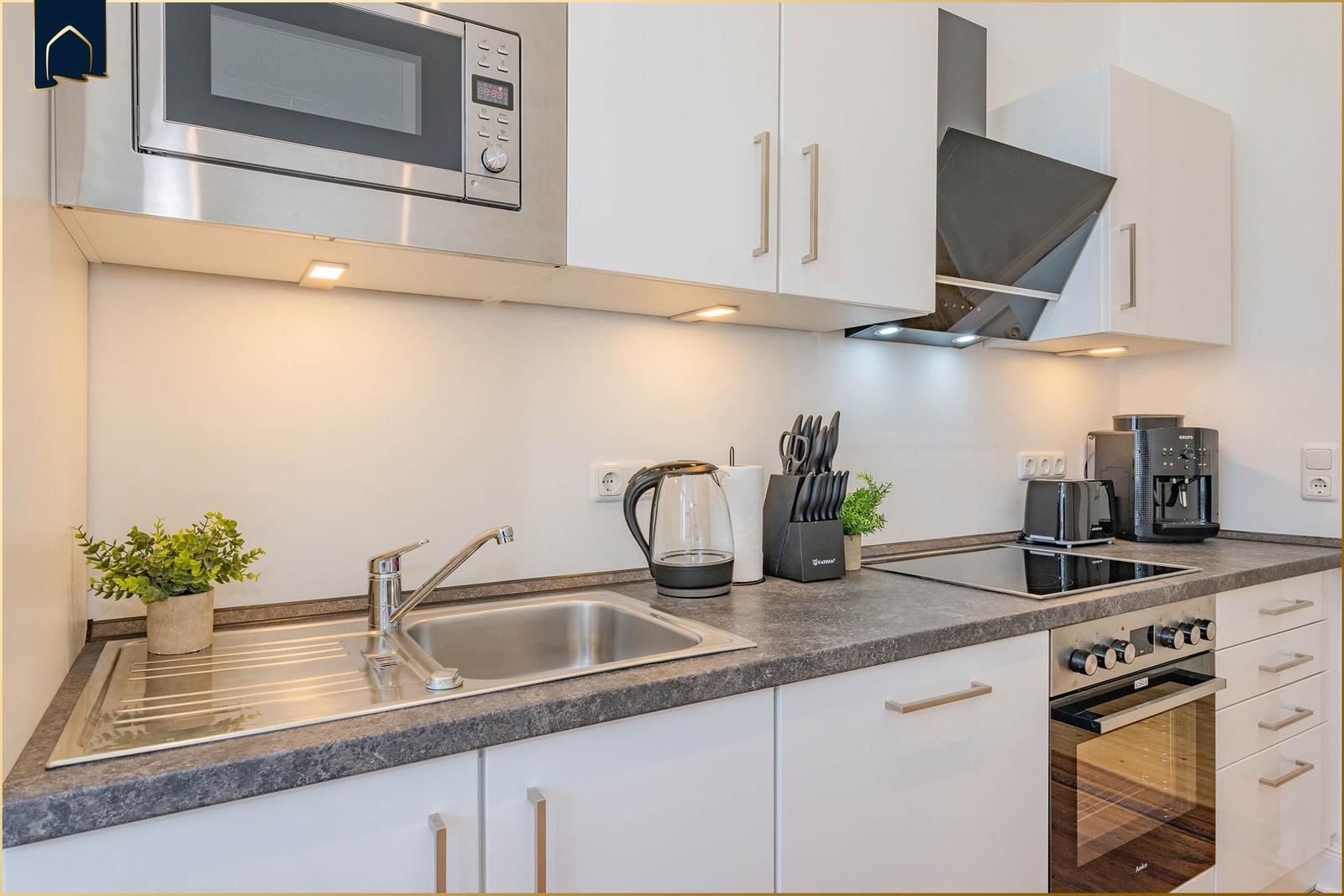 Küche mit Spüle, Herd, Dunstabzug und Mikrowelle.