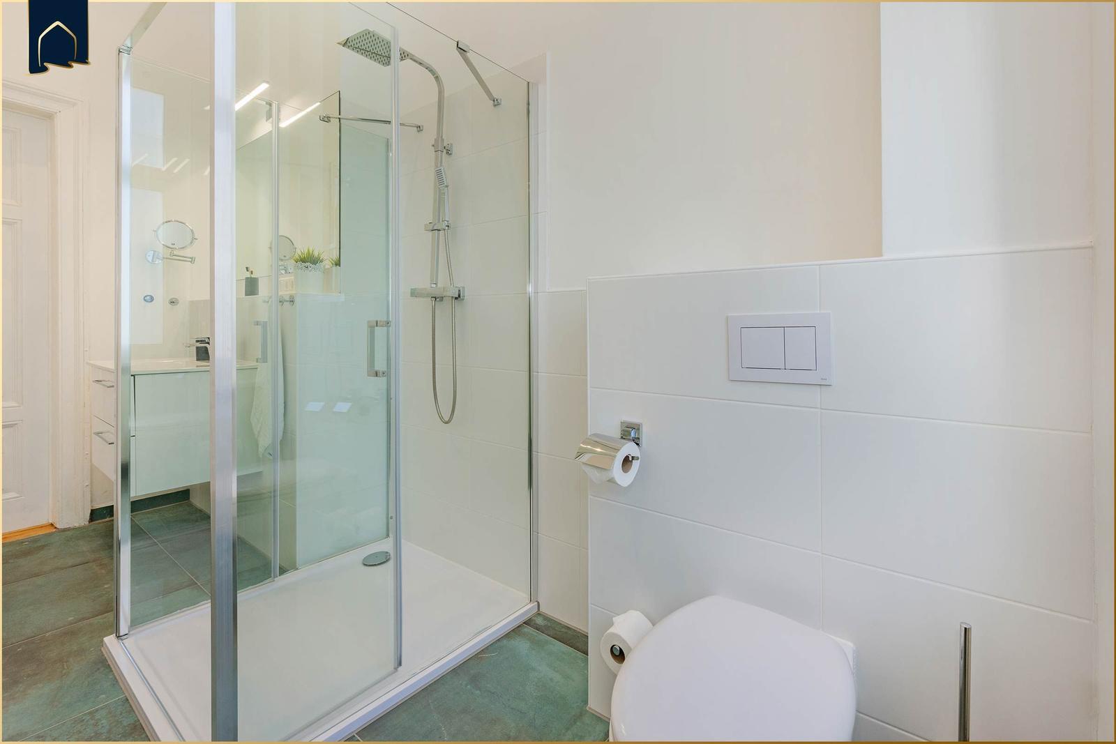 Duschkabine mit Glaswand, Toilette und Toilettenpapierhalter an der Wand.