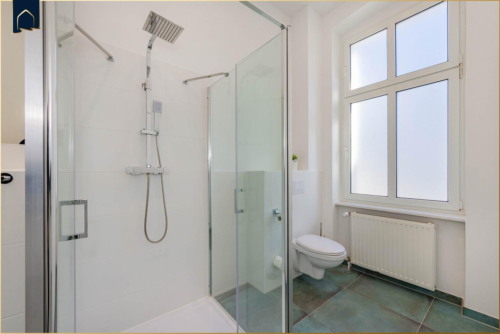 Dusche mit Glaswand, Toilette und Fenster mit Heizkörper.