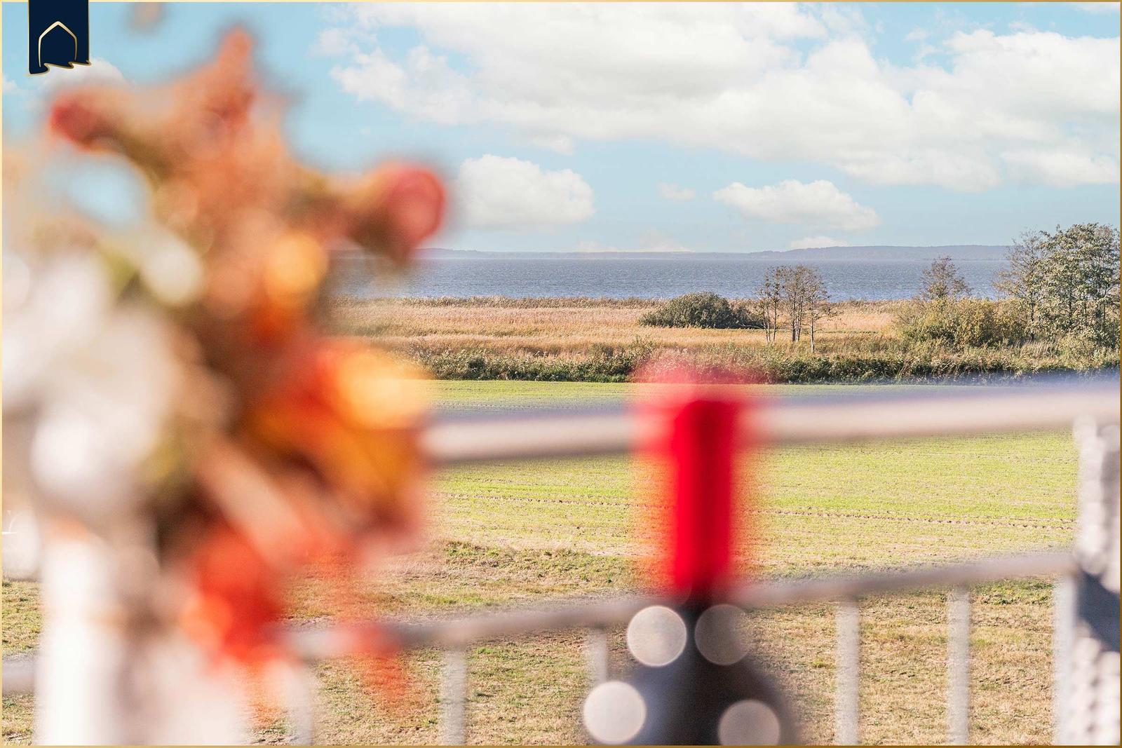 Von der Terrasse bietet sich ein Blick auf Felder und Meer unter blauem Himmel mit Wolken.