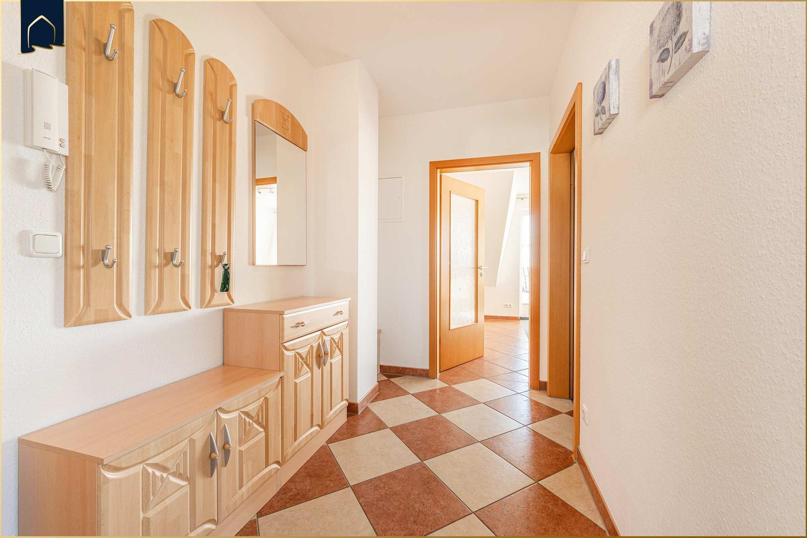 Flur mit Holzgarderobe, Spiegeln und gefliestem Boden. Türen führen in weitere Räume.