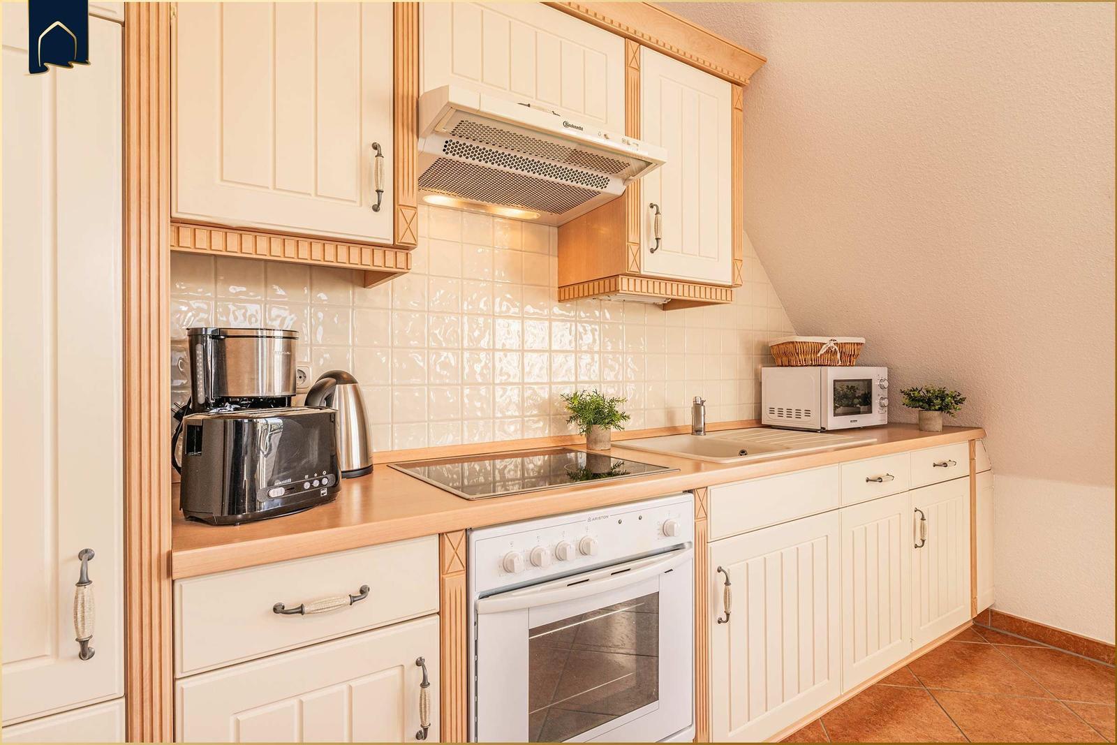 Küche mit weißen Schränken, Herd, Dunstabzug und Arbeitsfläche.