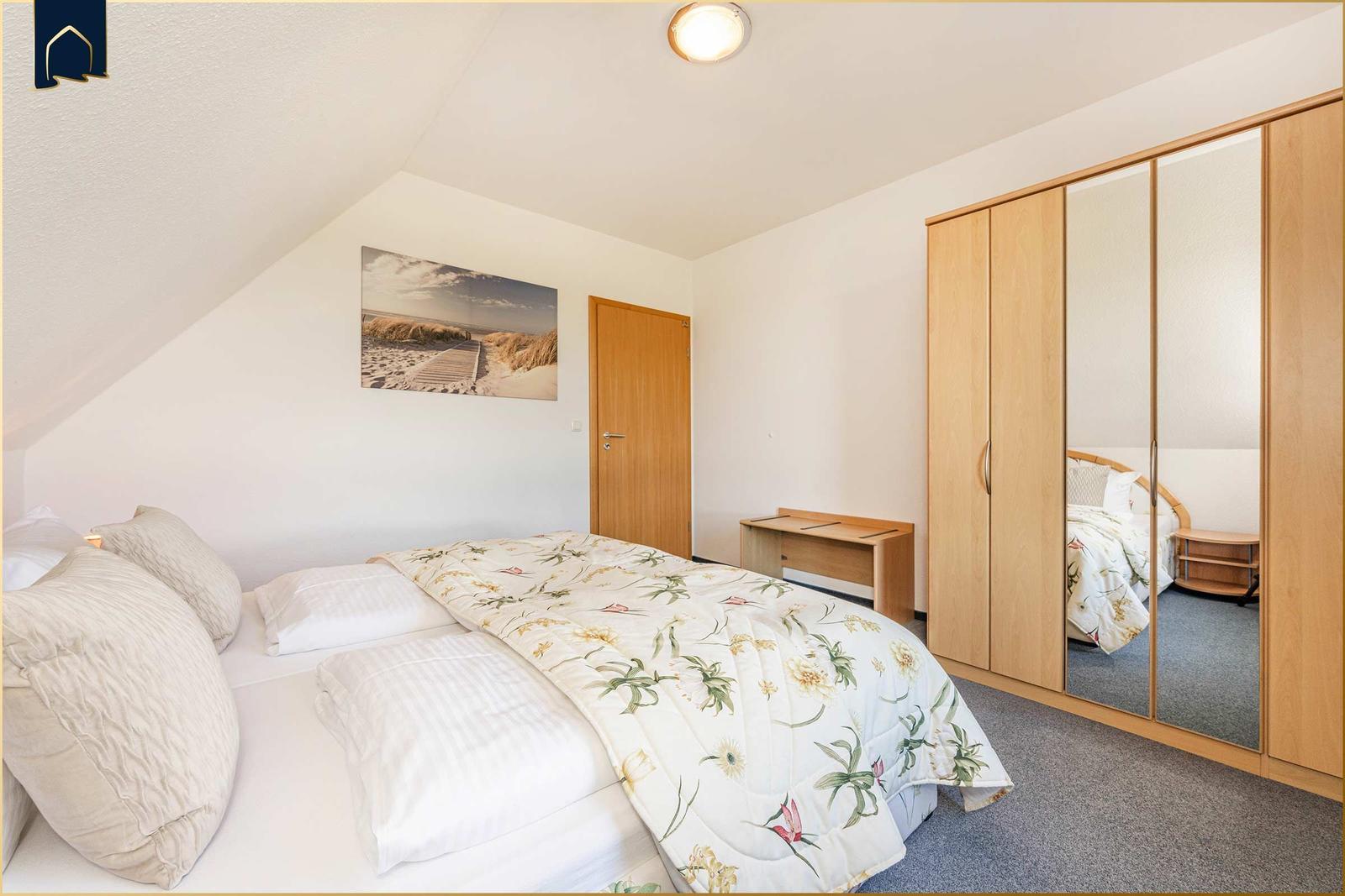 Schlafzimmer mit Bett, Kleiderschrank und Wandbild.