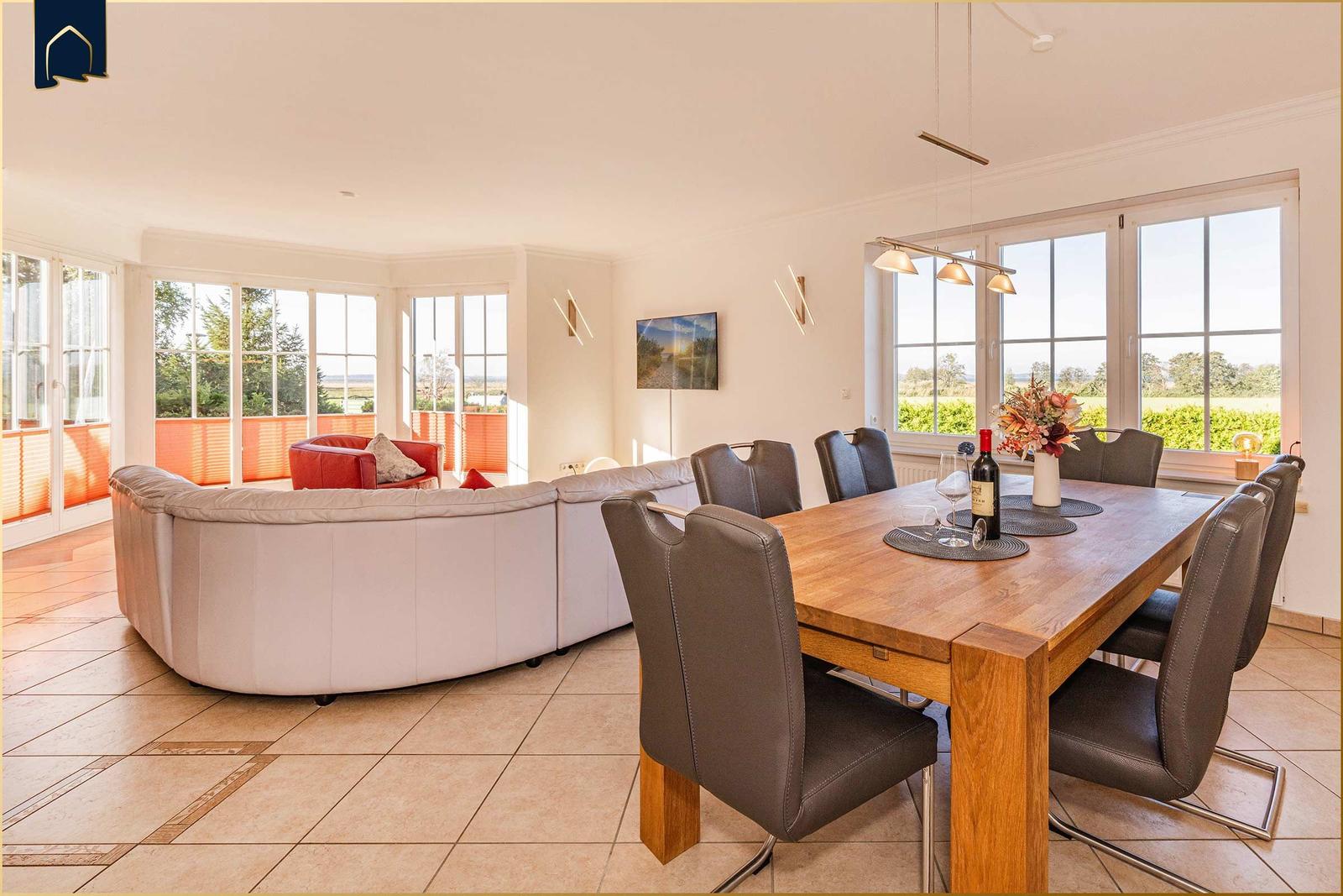 Großer Essbereich mit Holztisch und Stühlen. Wohnbereich mit Sofa und Fenstern.