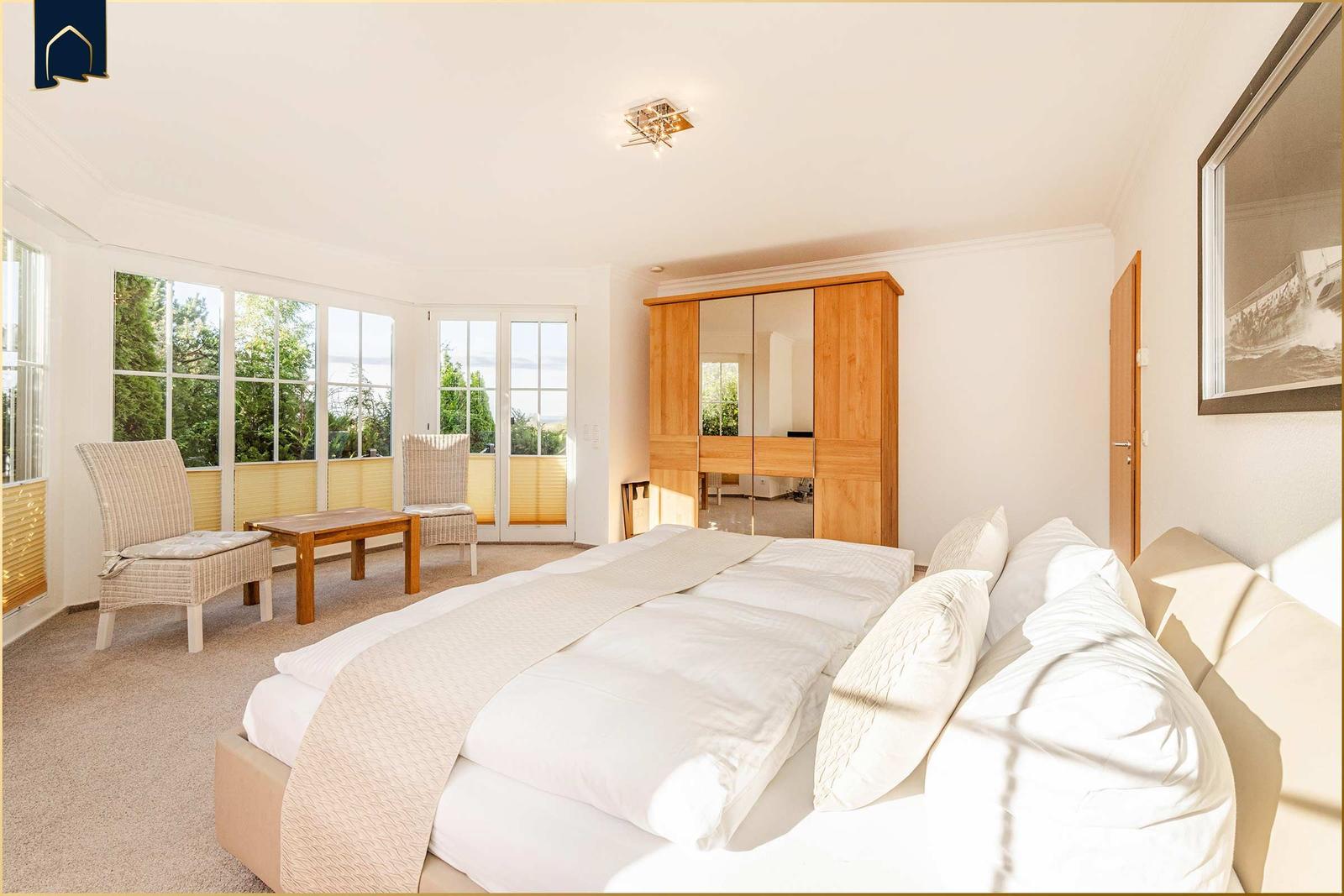 Schlafzimmer mit Doppelbett, Kleiderschrank und Sitzbereich mit Blick auf Garten.