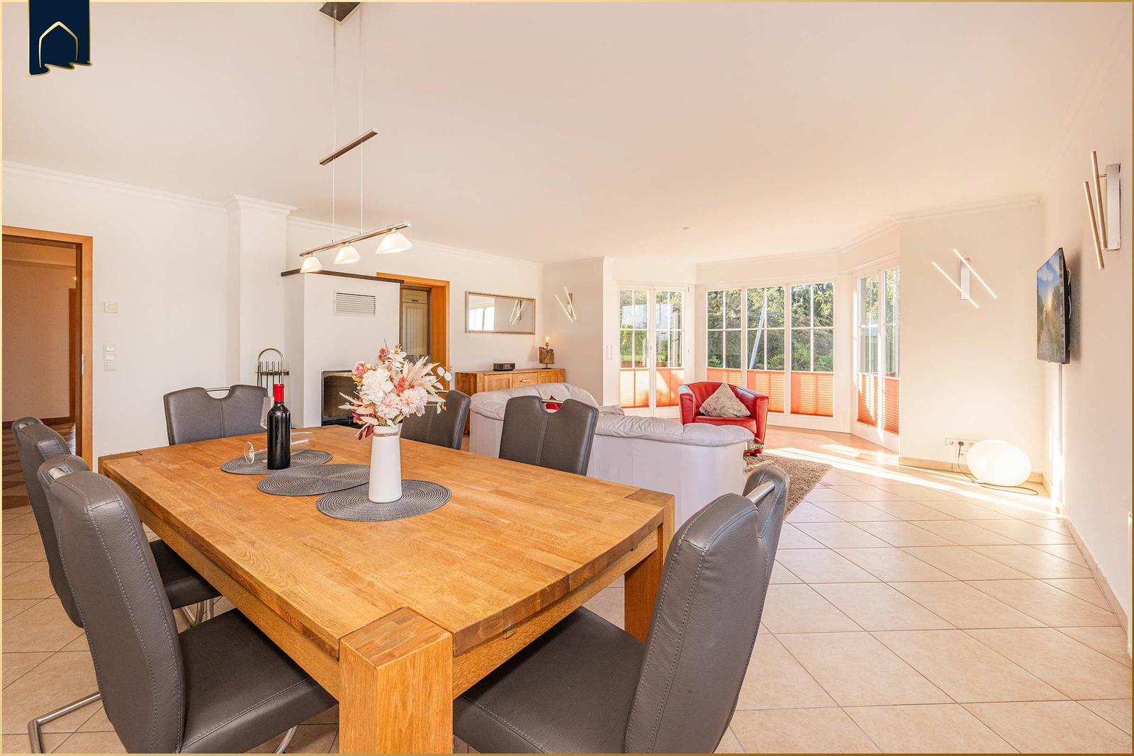 Esszimmer mit Holztisch und Stühlen. Wohnbereich mit Sofa und rotem Sessel.