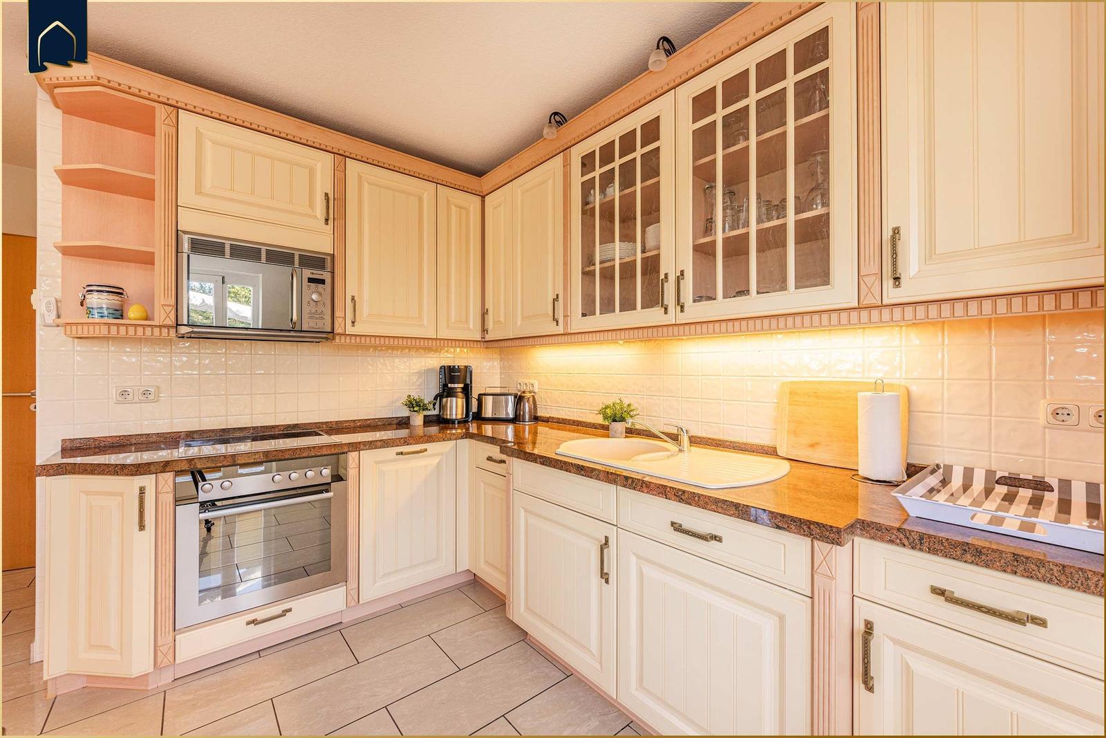 Küche mit hellen Schränken, Edelstahlgeräten und Steinarbeitsplatten.