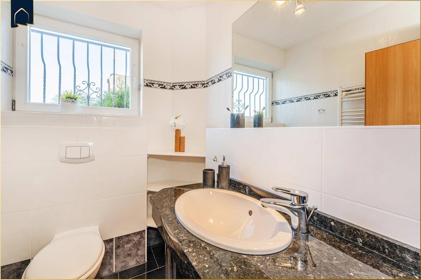 Bad mit Waschbecken, Toilette und Fenster mit Gitter.