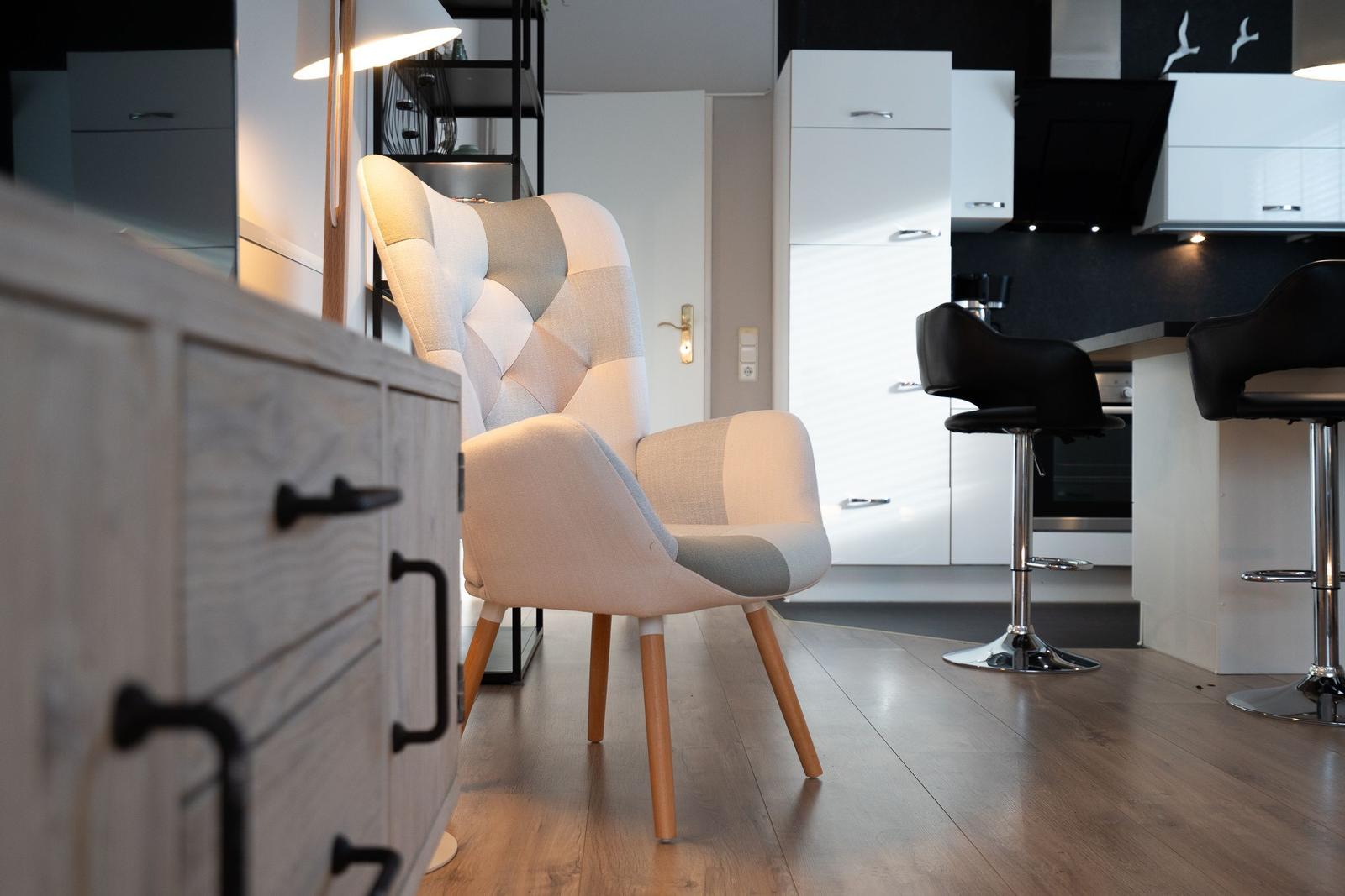 Ein Sessel mit Holzbeinen steht im Wohnbereich neben einer Küchenzeile mit Barhockern.