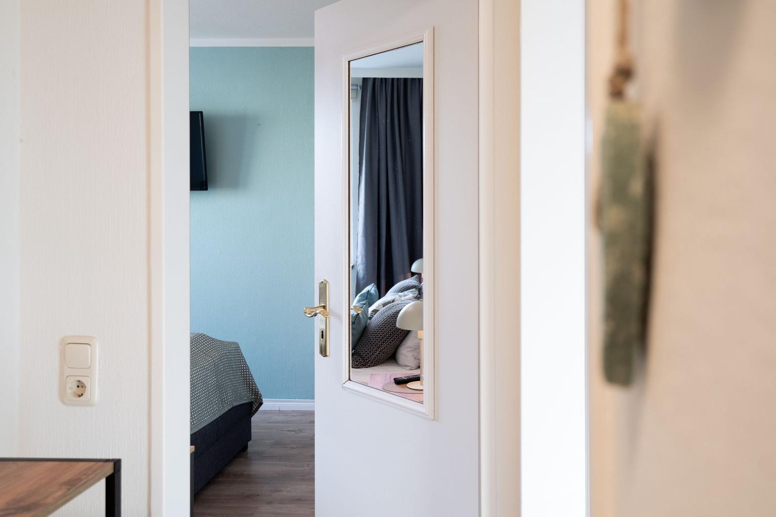 Schlafzimmer mit Bett, Wandfernseher und Spiegel an der Tür.