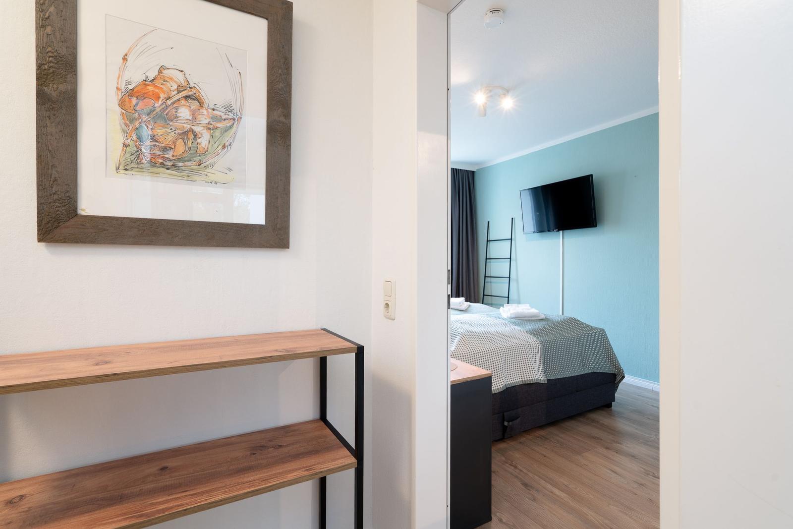 Schlafzimmer mit Bett, TV und Holzboden. An der Wand hängt ein Bild in einem Holzrahmen.