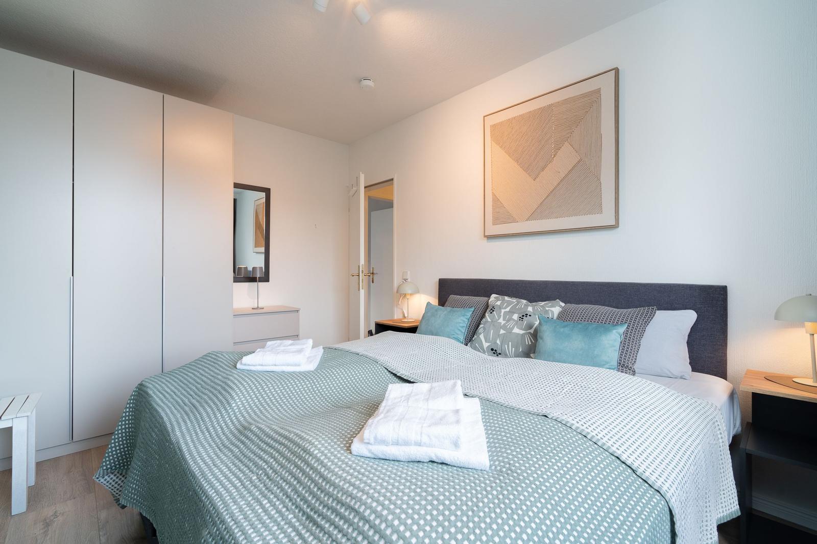 Schlafzimmer mit Bett, Nachttischen und Kleiderschrank. Auf dem Bett liegen Handtücher.