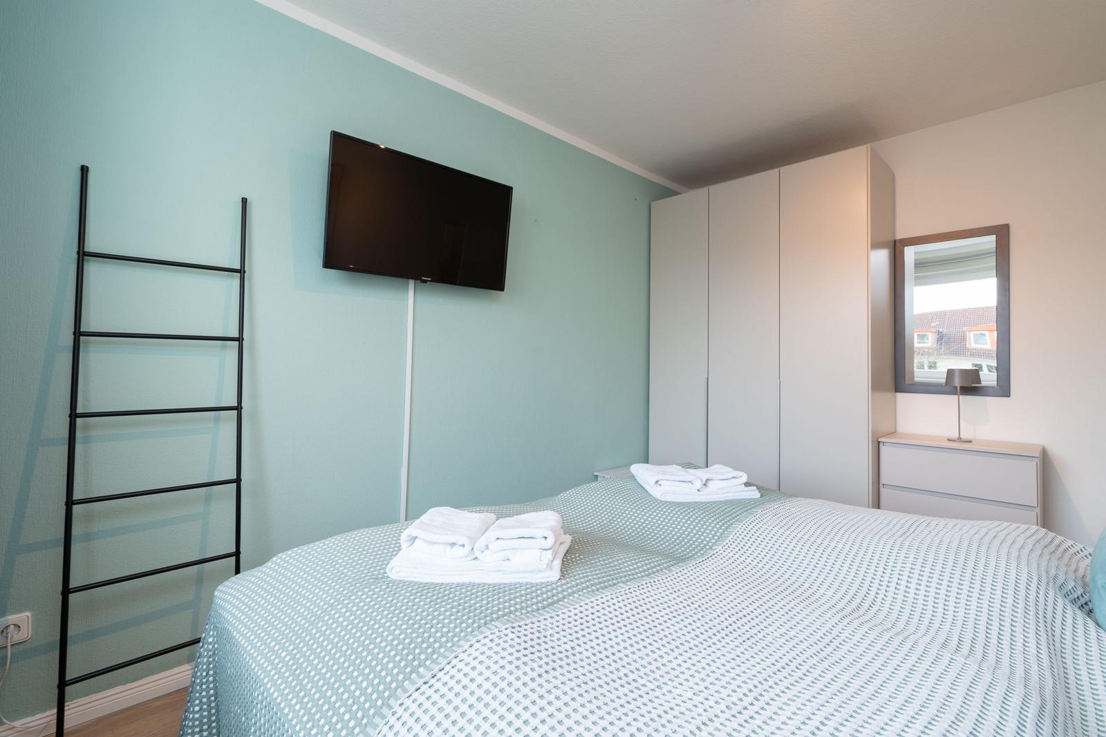 Schlafzimmer mit Bett, Fernseher, Kleiderschrank und Spiegel.