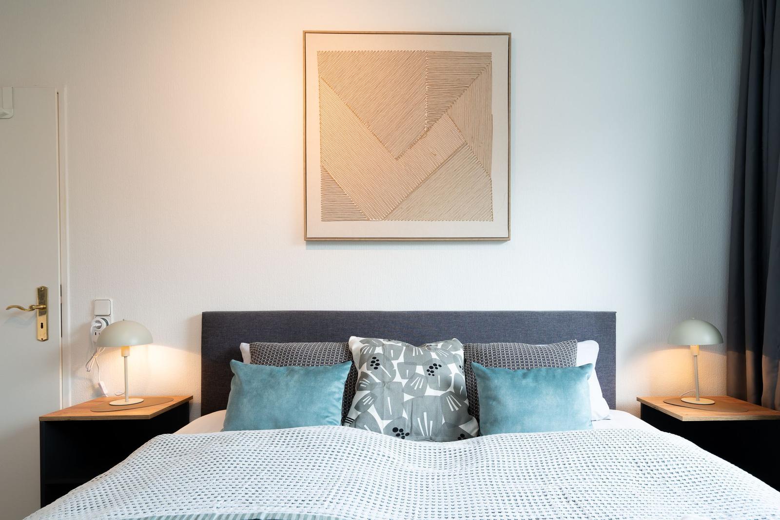 Schlafzimmer mit Bett, Nachttischen und Wandbild.