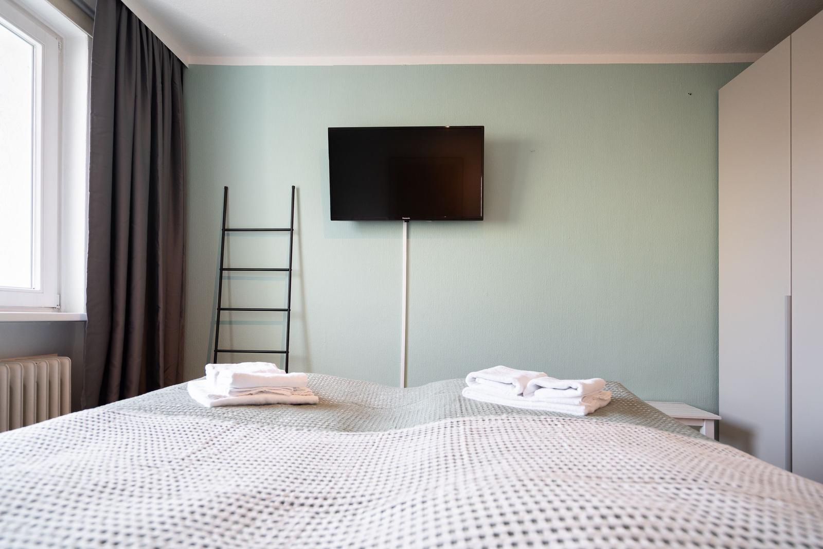 Schlafzimmer mit Bett, Fernseher und Fenster. Handtücher auf dem Bett.