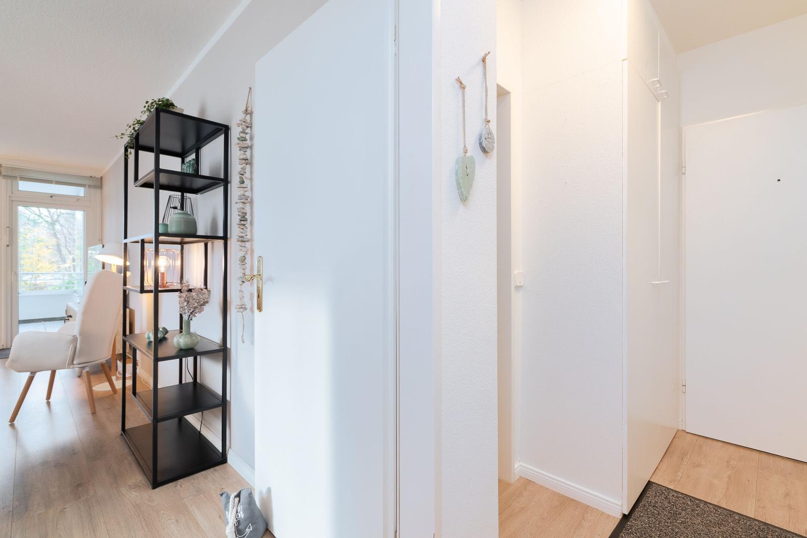 Eingangsbereich mit schwarzer Regalwand, Tür und Holzboden. Dekorative Elemente an der Wand.