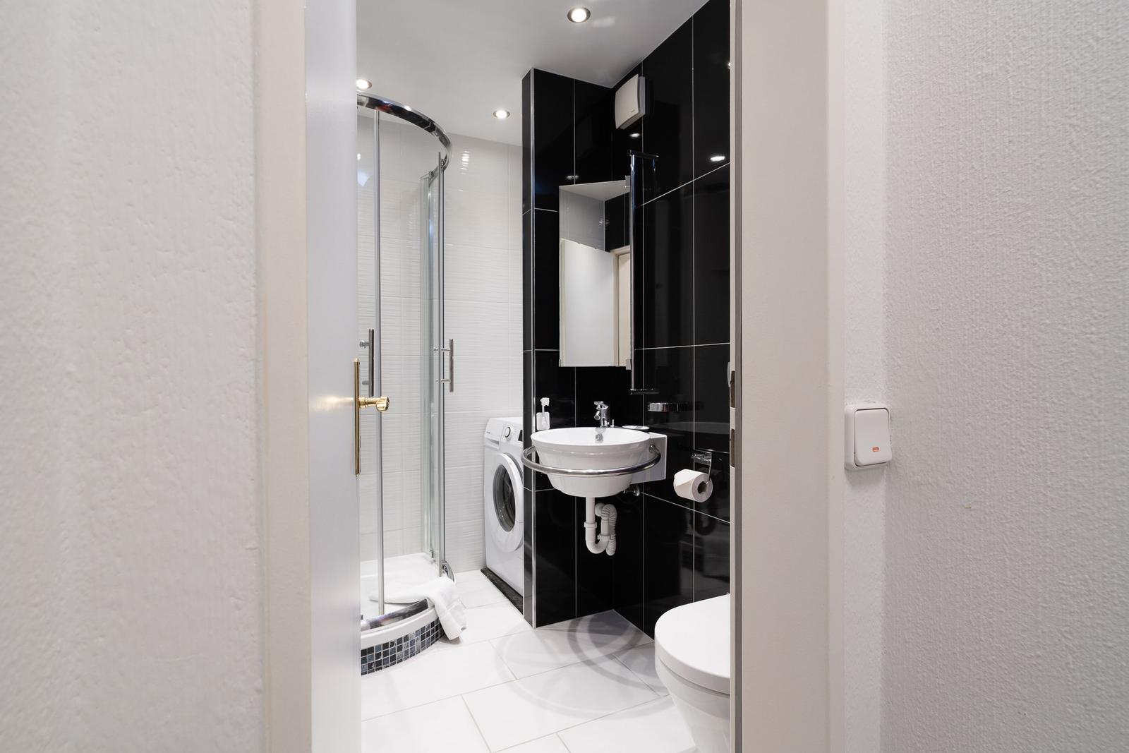 Badezimmer mit Dusche, Waschmaschine und Toilette. Schwarze und weiße Fliesen.