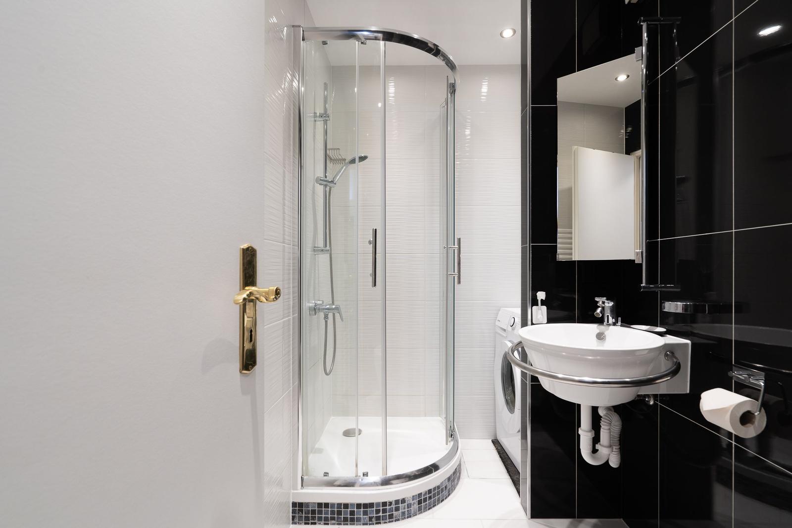 Badezimmer mit Duschkabine, Waschbecken und Waschmaschine.