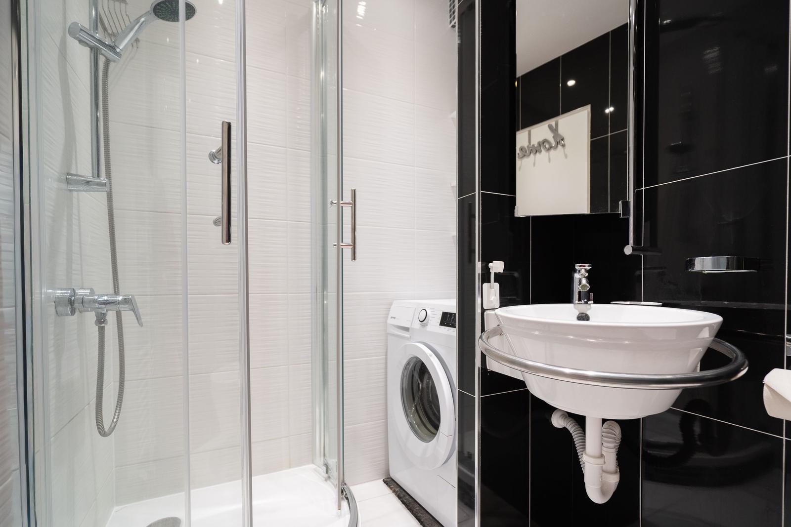 Badezimmer mit Dusche, Waschmaschine und Waschbecken.