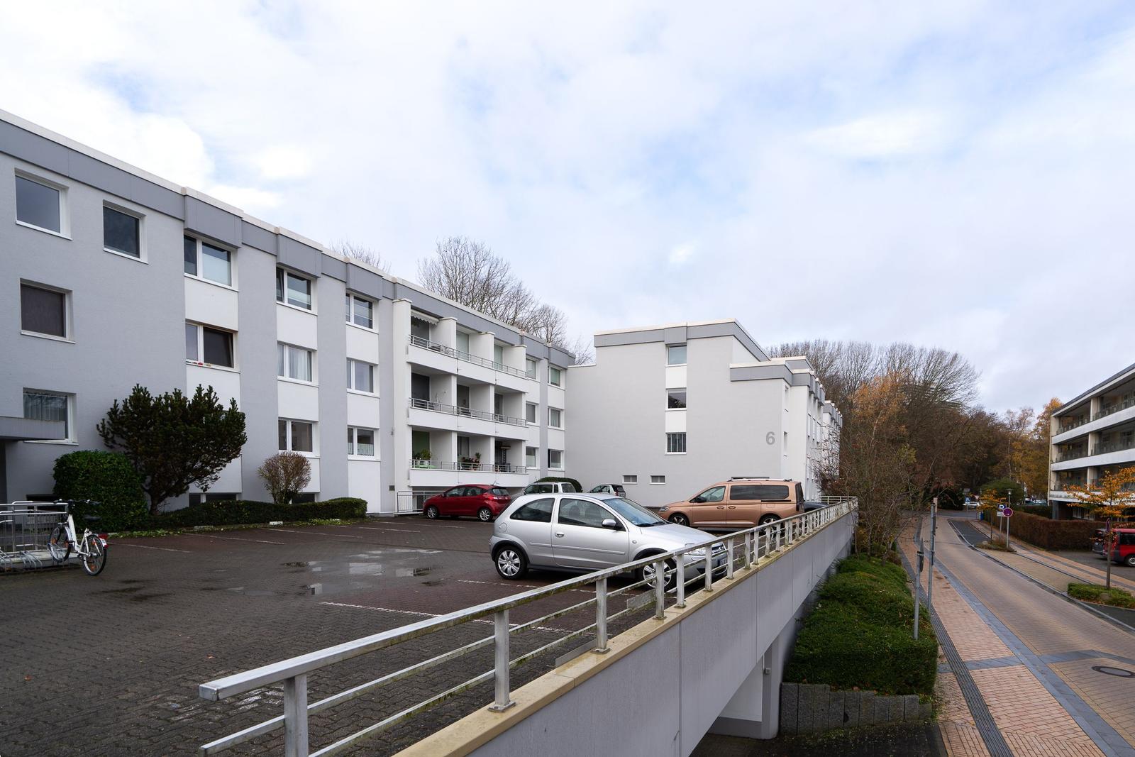 Modernes Mehrfamilienhaus mit Parkplatz und Bäumen im Hintergrund.