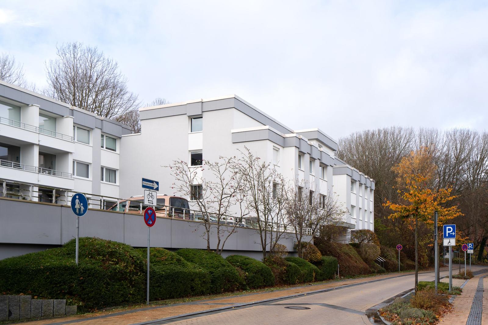 Moderne Wohnanlage mit Balkonen und Parkplatzanlagen. Bäume und Beete säumen die Straße.