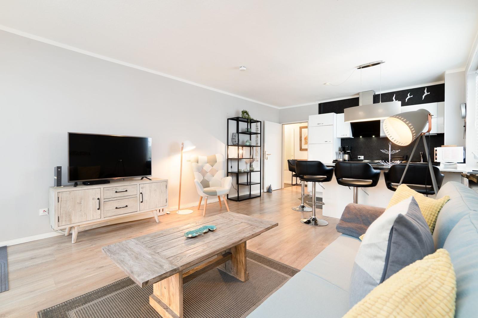 Wohnzimmer mit Sofa, Couchtisch, Fernseher und offener Küche mit Barhockern.