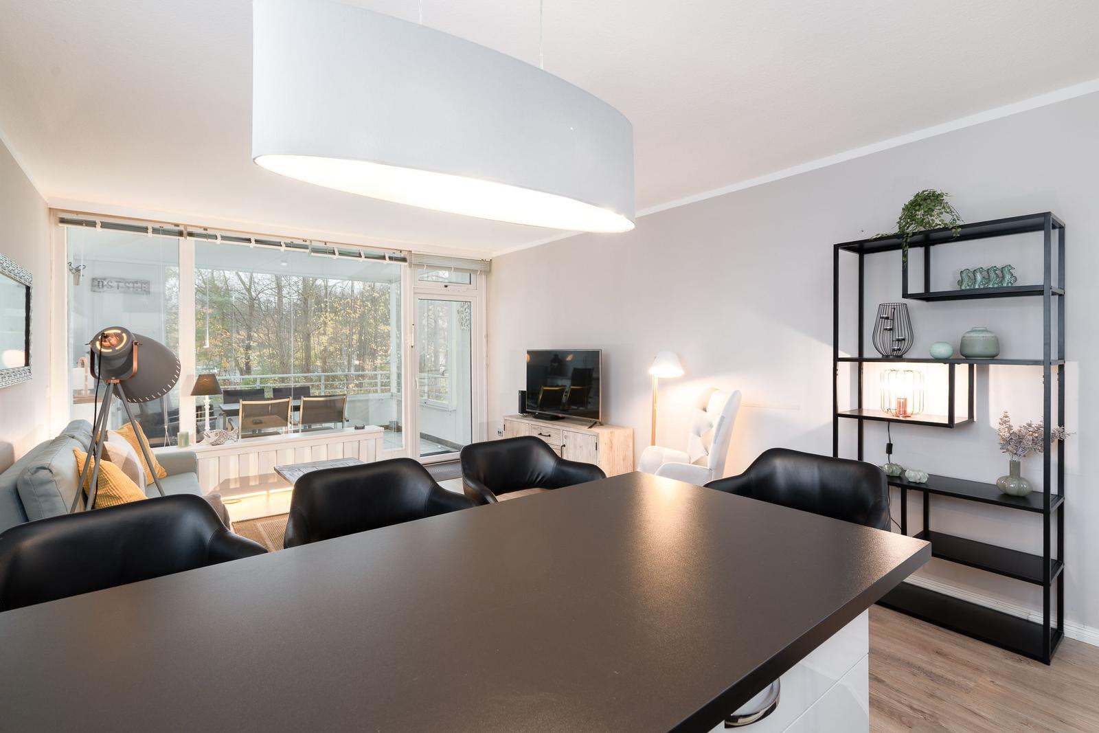 Wohn- und Essbereich mit schwarzen Stühlen, TV und Regal. Durchgang zur Terrasse.