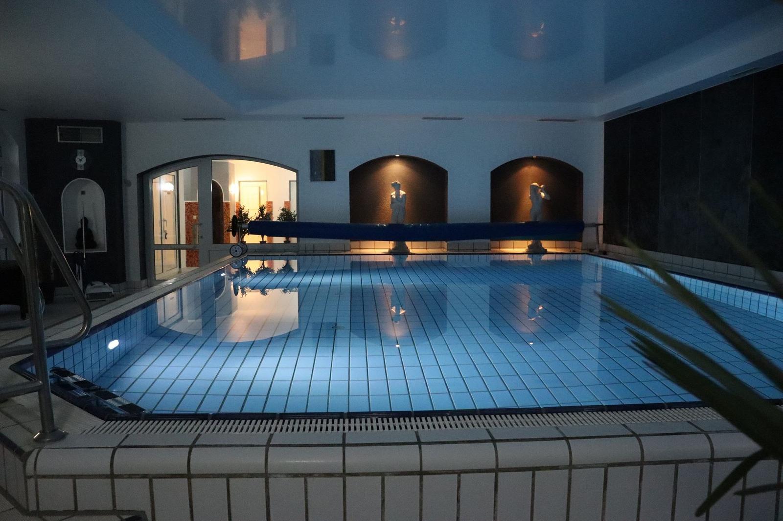 Innere Schwimmbad mit beleuchteten Fliesen und Statuen an der Wand.