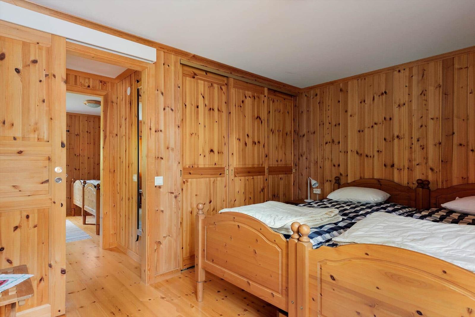 Zimmer mit Holzwand und zwei Betten. Tür führt in einen weiteren Raum.