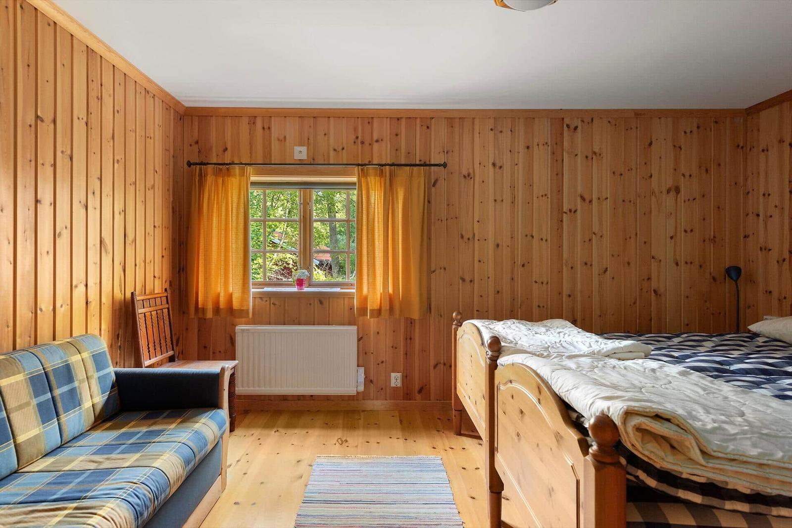 Schlafzimmer mit Holzwand, Bett, Sofa und Fenster mit Vorhängen.