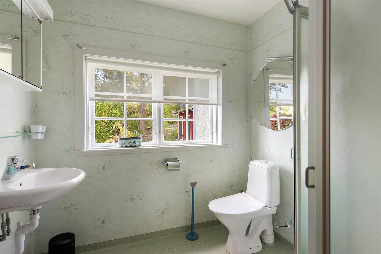 Badezimmer mit Toilette, Waschbecken und Fenster mit Blick nach draußen.
