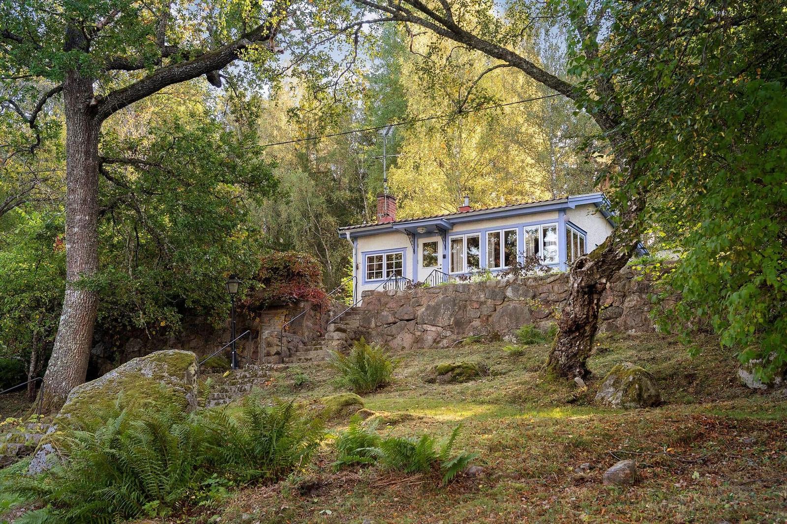 Ein Haus mit blauen Fensterrahmen steht inmitten von Bäumen und Steinen.