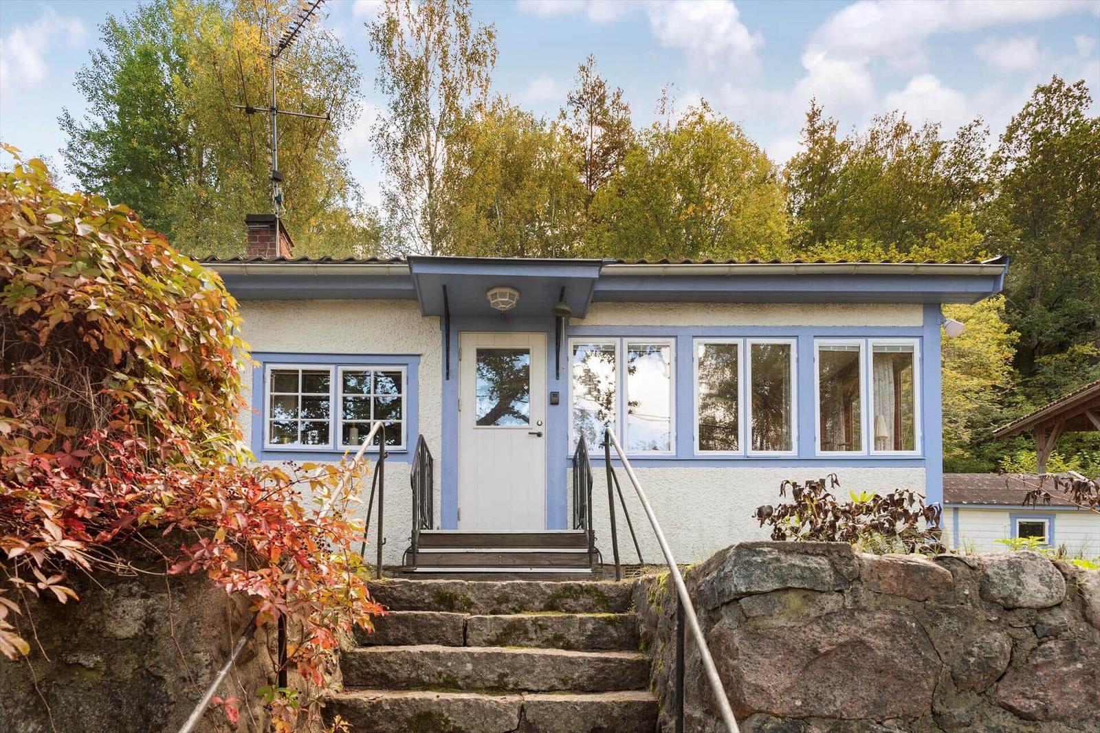 Ein Haus mit blauen Fensterrahmen und weißer Tür. Treppen führen zur Eingangstür.