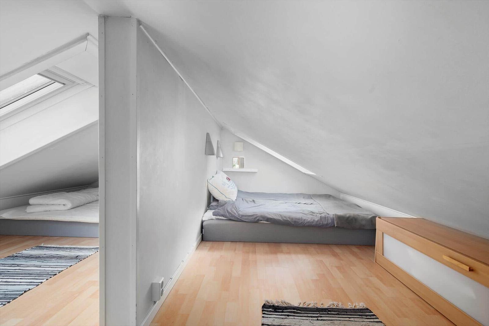 Zimmer mit Dachschrägen, Bett und Holzboden. Fenster und Kleiderschrank sichtbar.