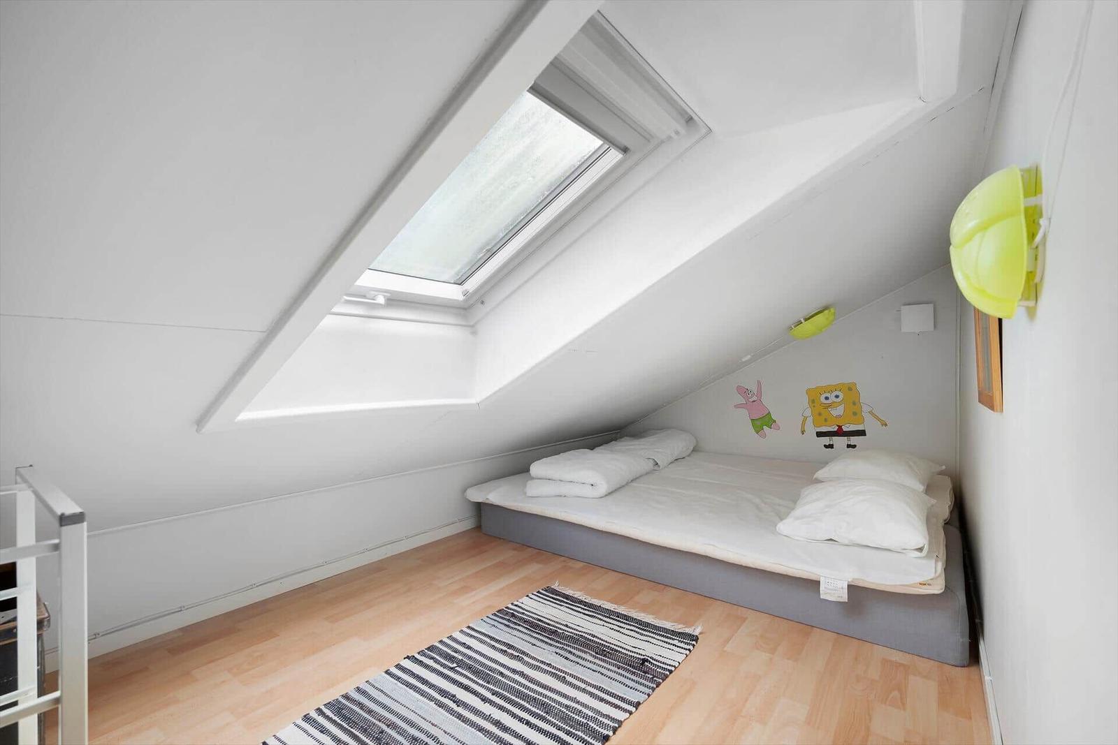 Dachgeschosszimmer mit Dachfenster, Matratze und Cartoon-Wanddekoration.